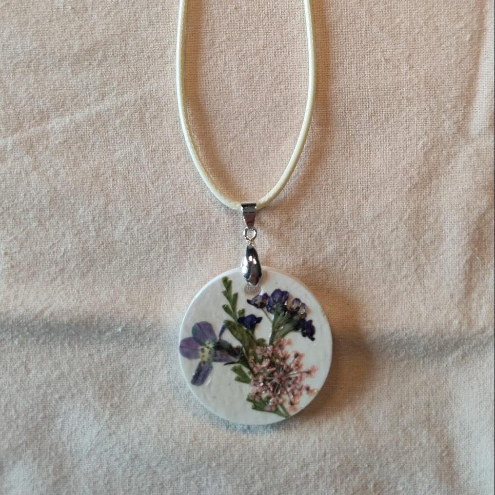 Collier médaillon rond en pierre blanche orné d'une ombelle rose poudré et de petites fleurs violettes séchées, monté sur cordon ciré écru — NERÉA